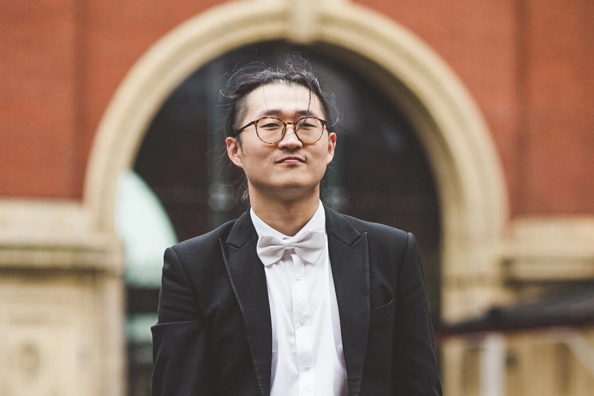 Wenhan Jiang standing in front of building in black suit jacket, white shirt and bow tie