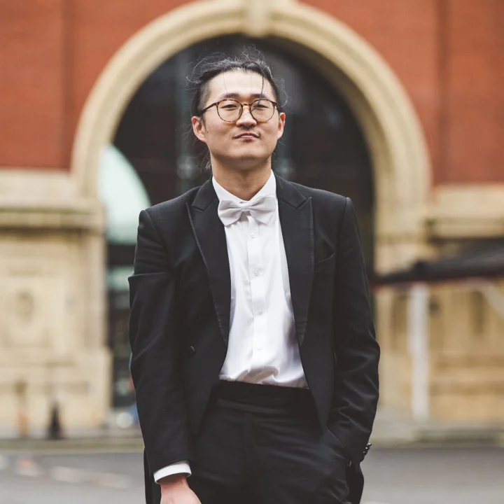 Wenhan Jiang standing in front of building in black suit jacket, white shirt and bow tie