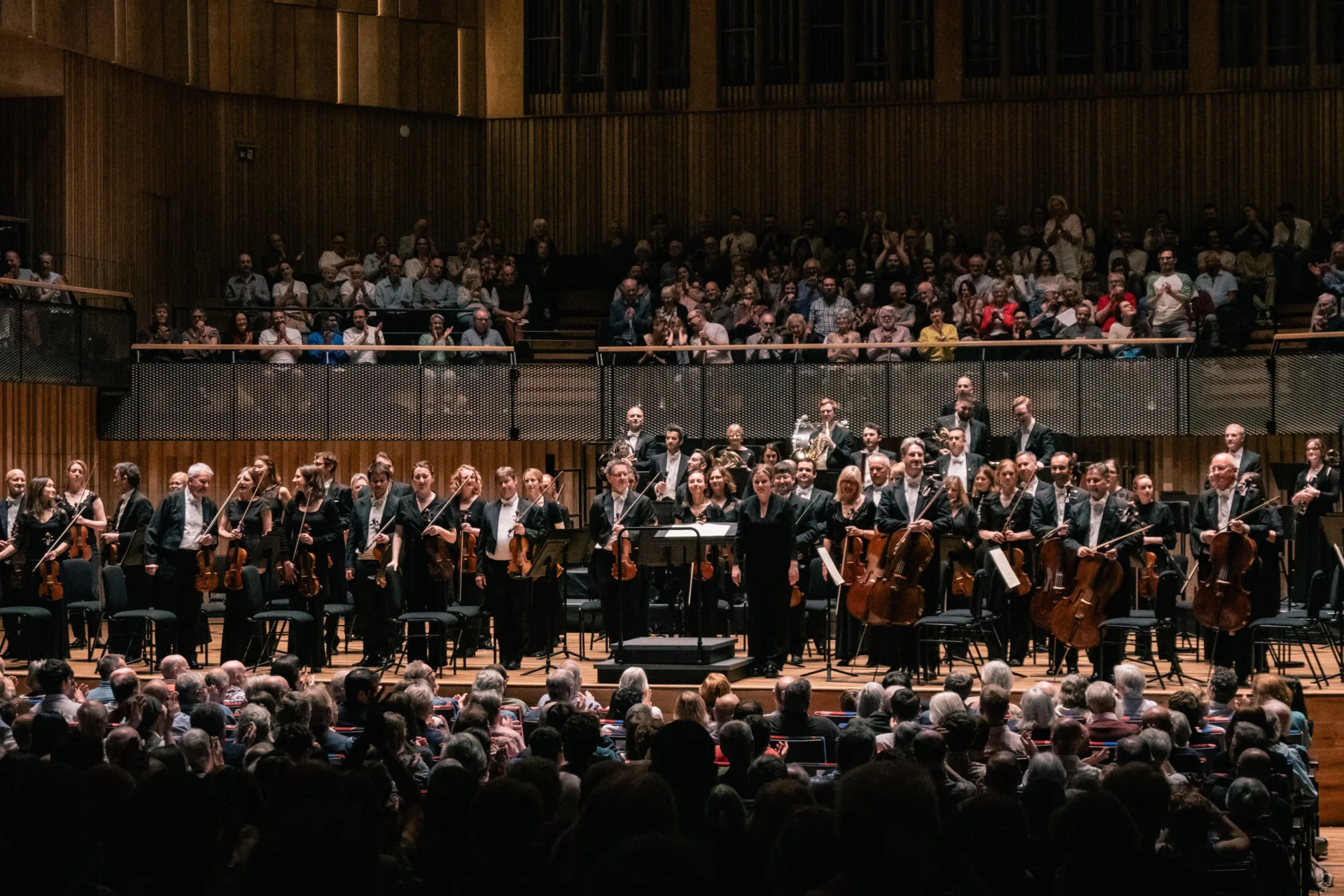 The Royal Philharmonic Orchestra stands on stage at the Bristol Beacon, receiving applause.