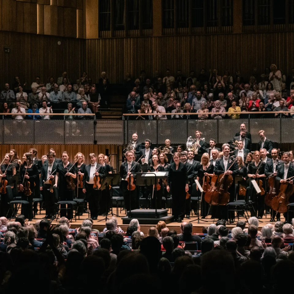 The Royal Philharmonic Orchestra stands on stage at the Bristol Beacon, receiving applause.