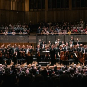 The Royal Philharmonic Orchestra stands on stage at the Bristol Beacon, receiving applause.