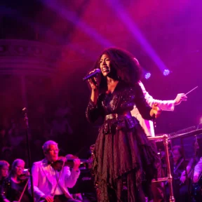 Gloria Onitiri stands singing in front of the Royal Philharmonic Orchestra