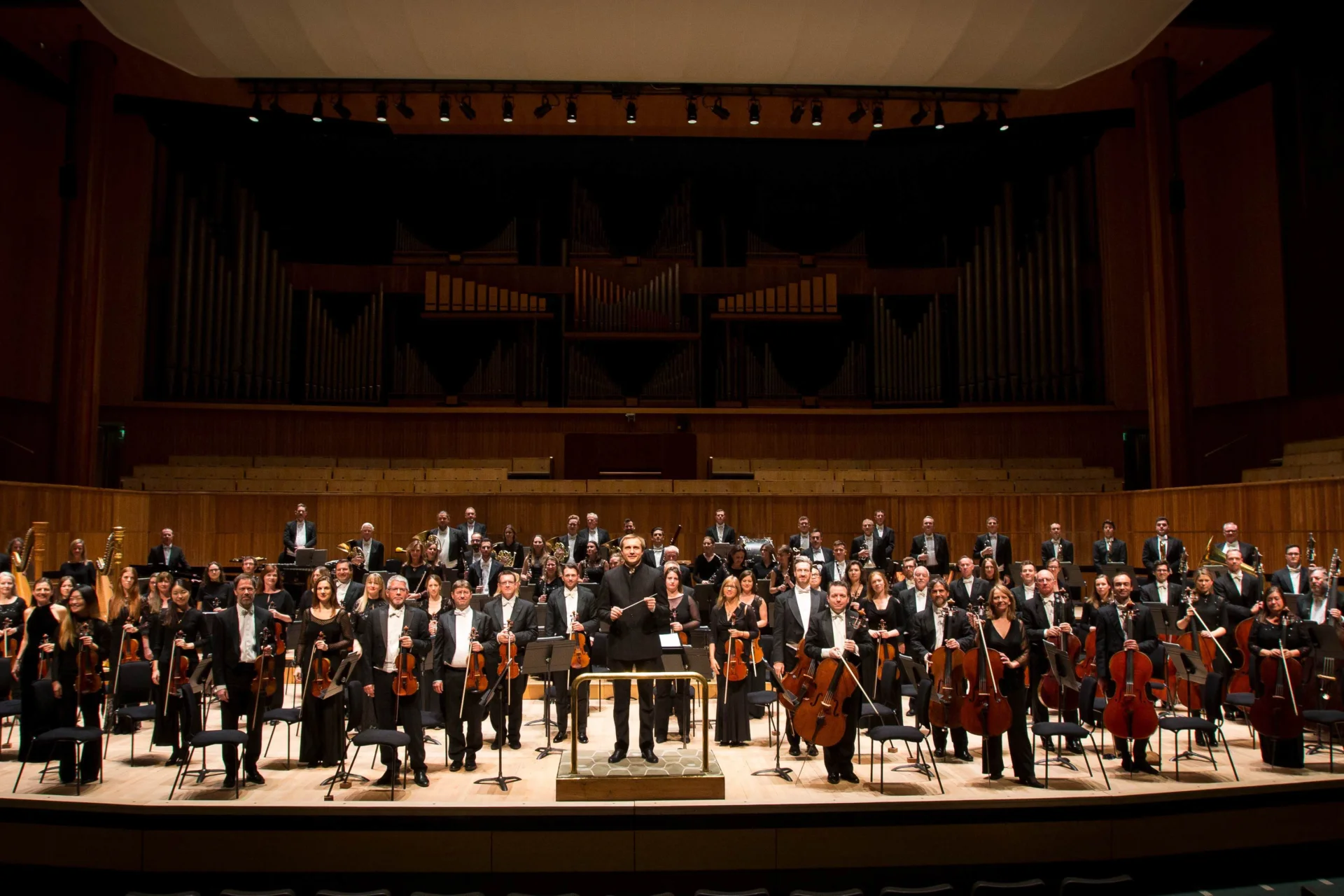 All of the Royal Philharmonic Orchestra stands on stage with their instruments, with conductor Vasily Petrenko in the middle