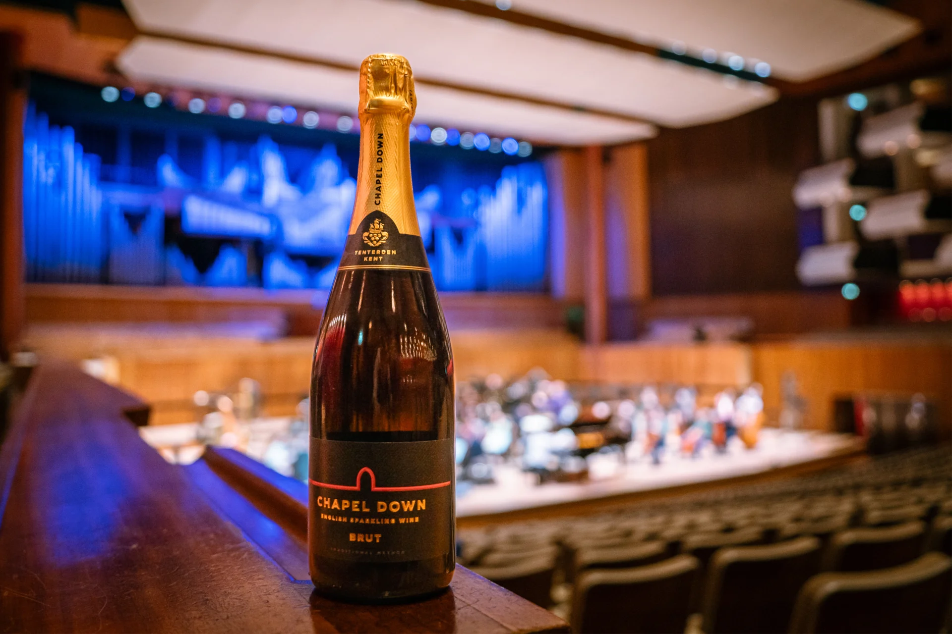 A bottle of Chapel Down on the left side stalls ledge at the Royal Festival Hall, with the Orchestra rehearsing in the background