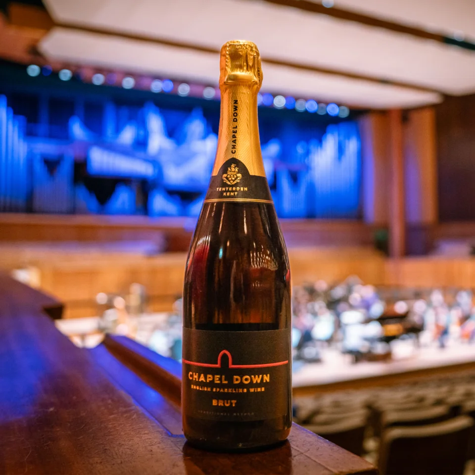 A bottle of Chapel Down on the left side stalls ledge at the Royal Festival Hall, with the Orchestra rehearsing in the background