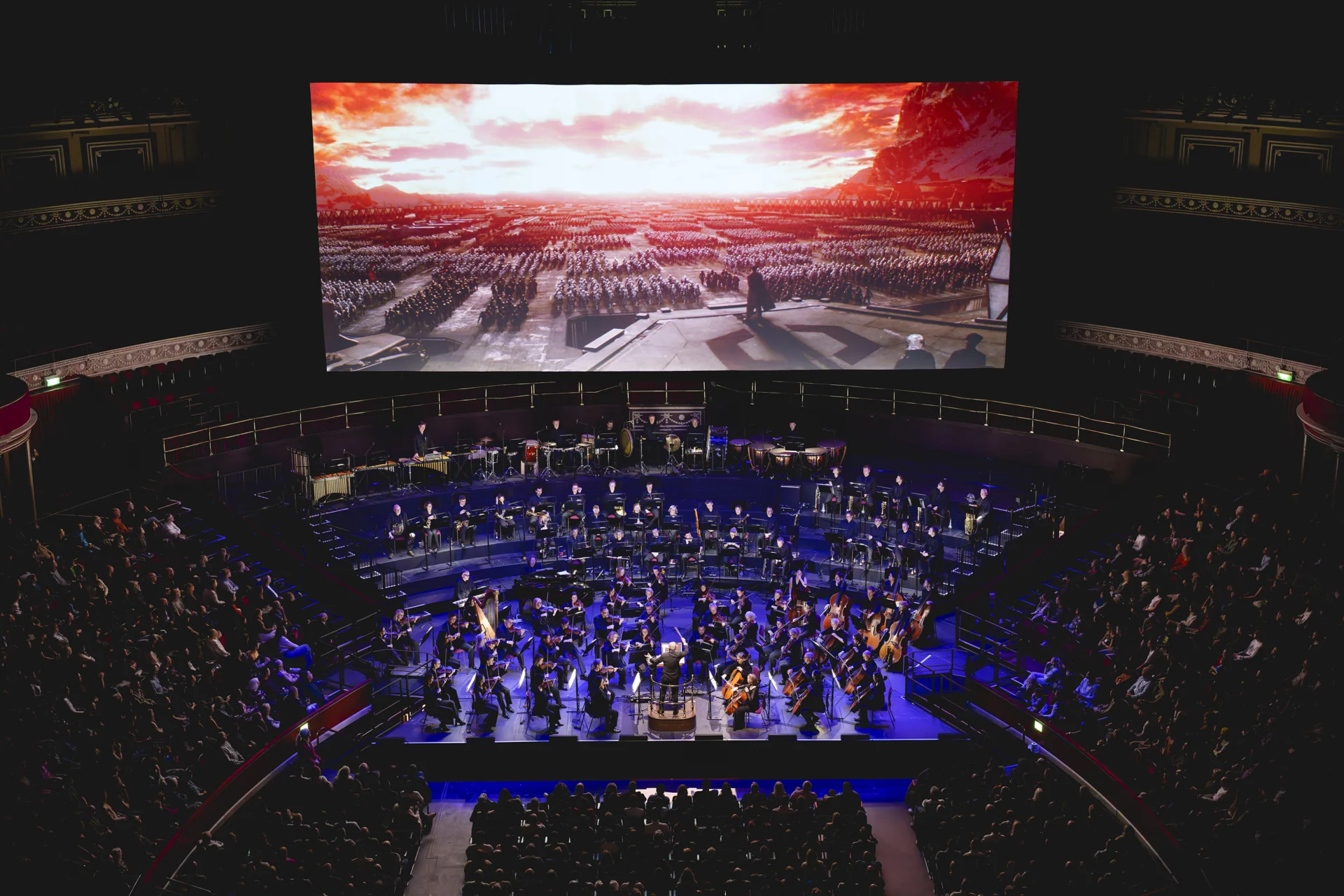 The RPCO performing on stage at the Royal Albert Hall under blue lighting with a scene from Star Wars projected on the screen behind them