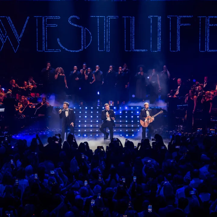 Three members of Westlife performing on stage at the Royal Albert Hall with the RPCO, singers and band to the sides