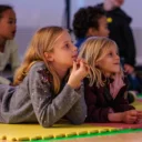 Two young girls lying on floor watching a performance