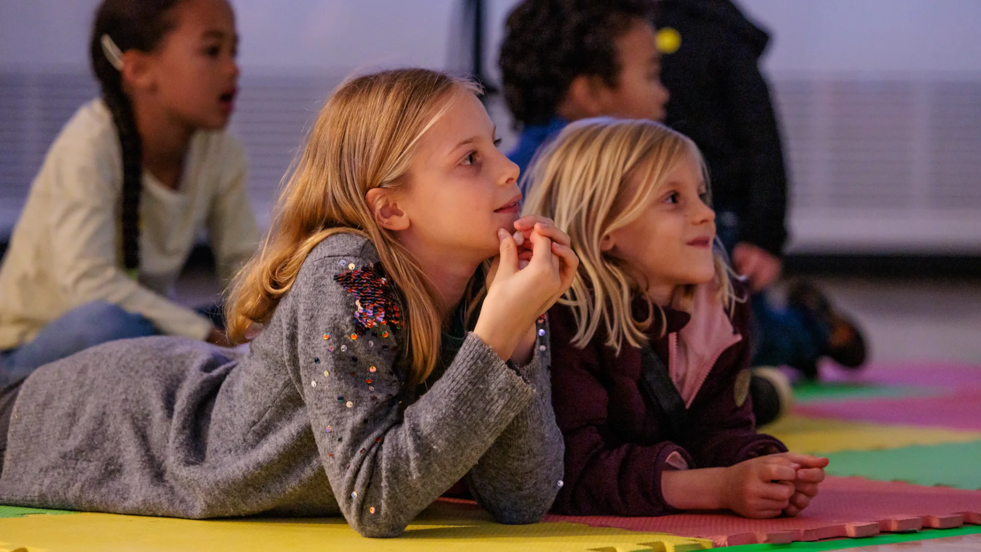 Two young girls lying on floor watching a performance