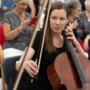 An RPO cellist at a STROKESTRA performance, looking to the side an raising her bow