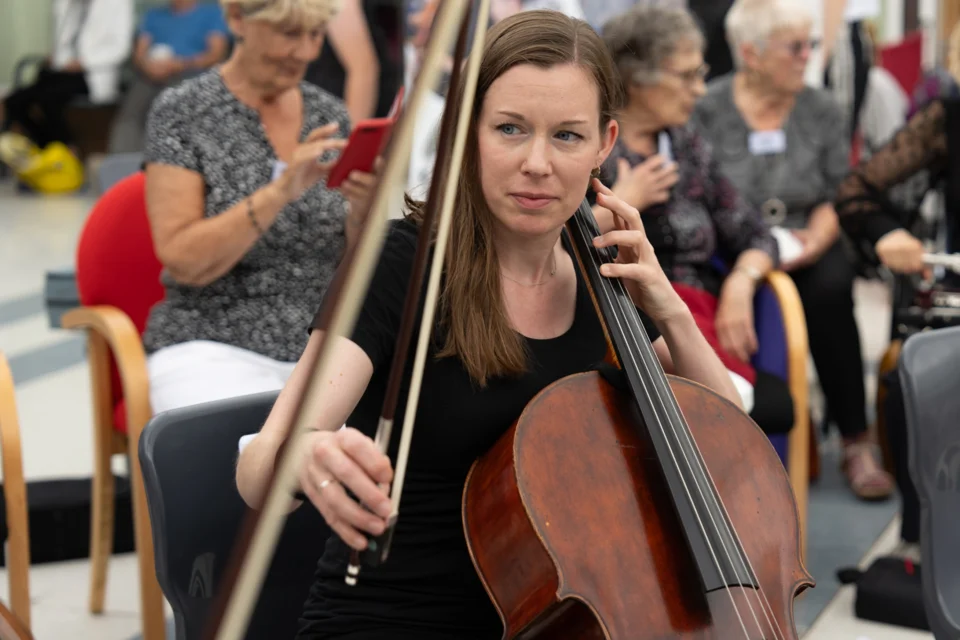 An RPO cellist at a STROKESTRA performance, looking to the side an raising her bow
