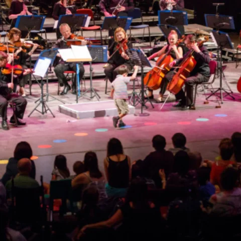 A child walks past the Royal Philharmonic Orchestra, hopping on coloured dots on the floor