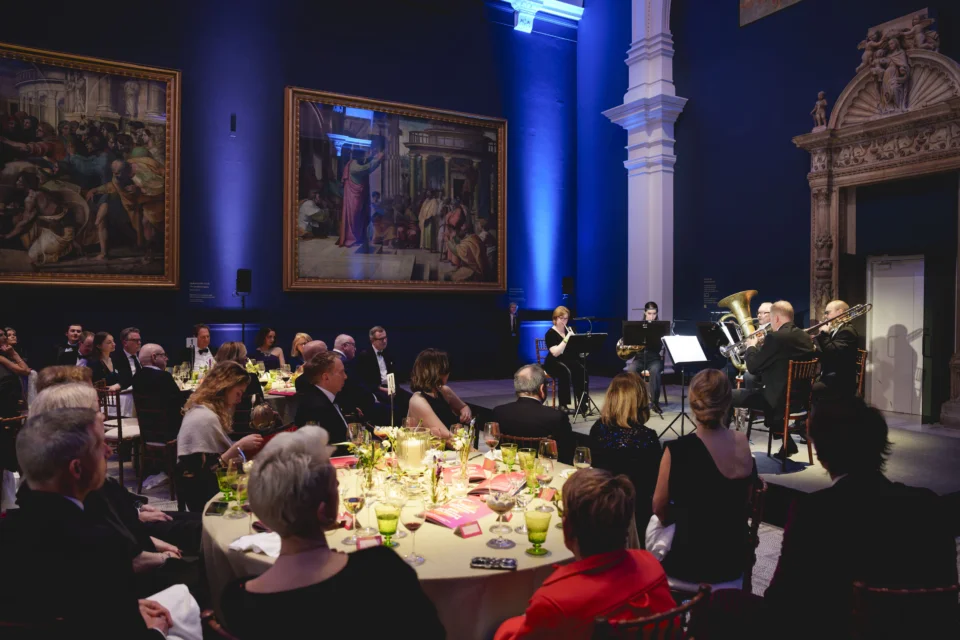 Attendees of the RPO's 80th Anniversary Gala Evening seated at dinner listening to the RPO Brass quintet performing surrounded by Raphael's cartoons in the Raphael Court of the V&A.