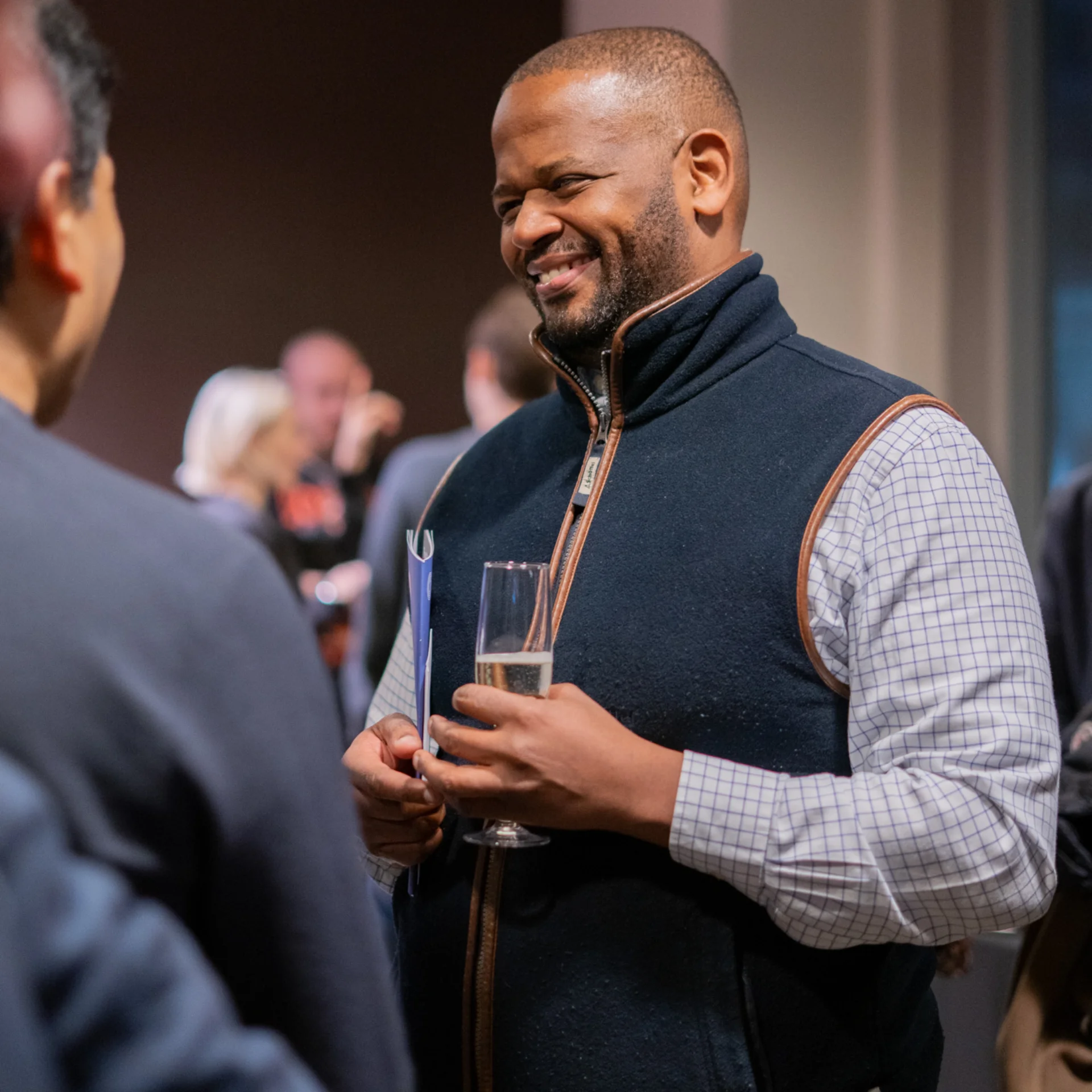Image of an RPO patron smiling whilst holding a glass of Chapel Down Sparkling wine and an RPO programme during an interval reception.