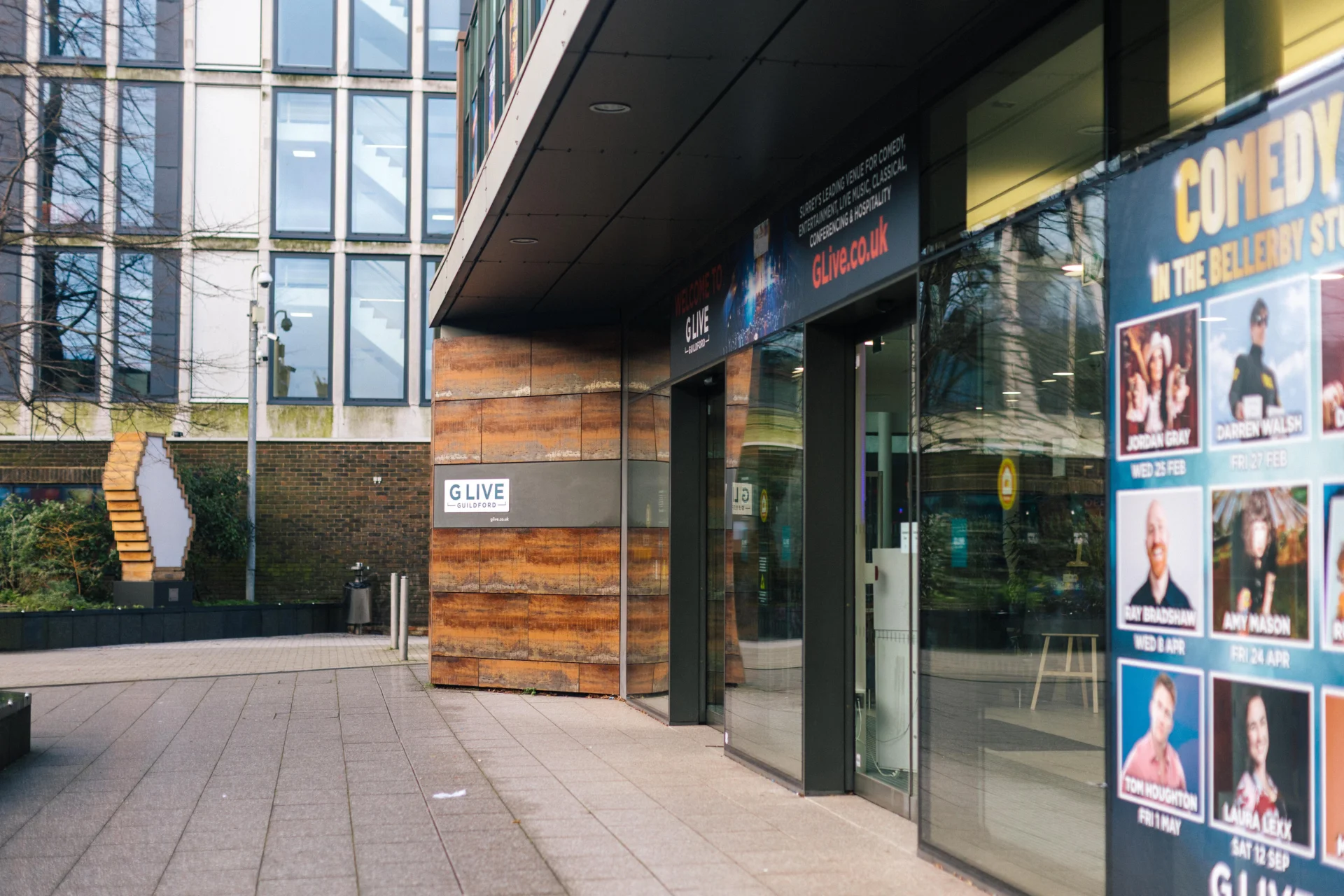 Close up shot of the entrance to G Live, a wooden wall next to two automatic glass doors