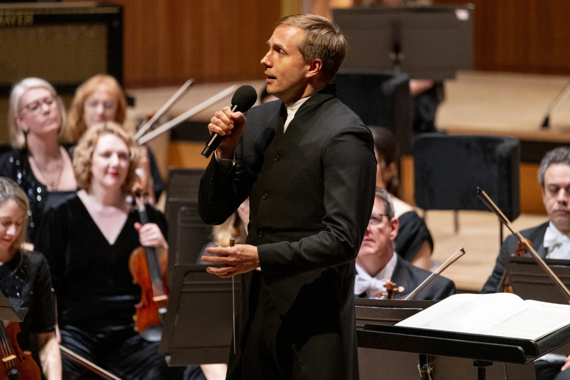 Vasily Petrenko stands ion stage in front of the Orchestra, speaking about the repertoire to the audience