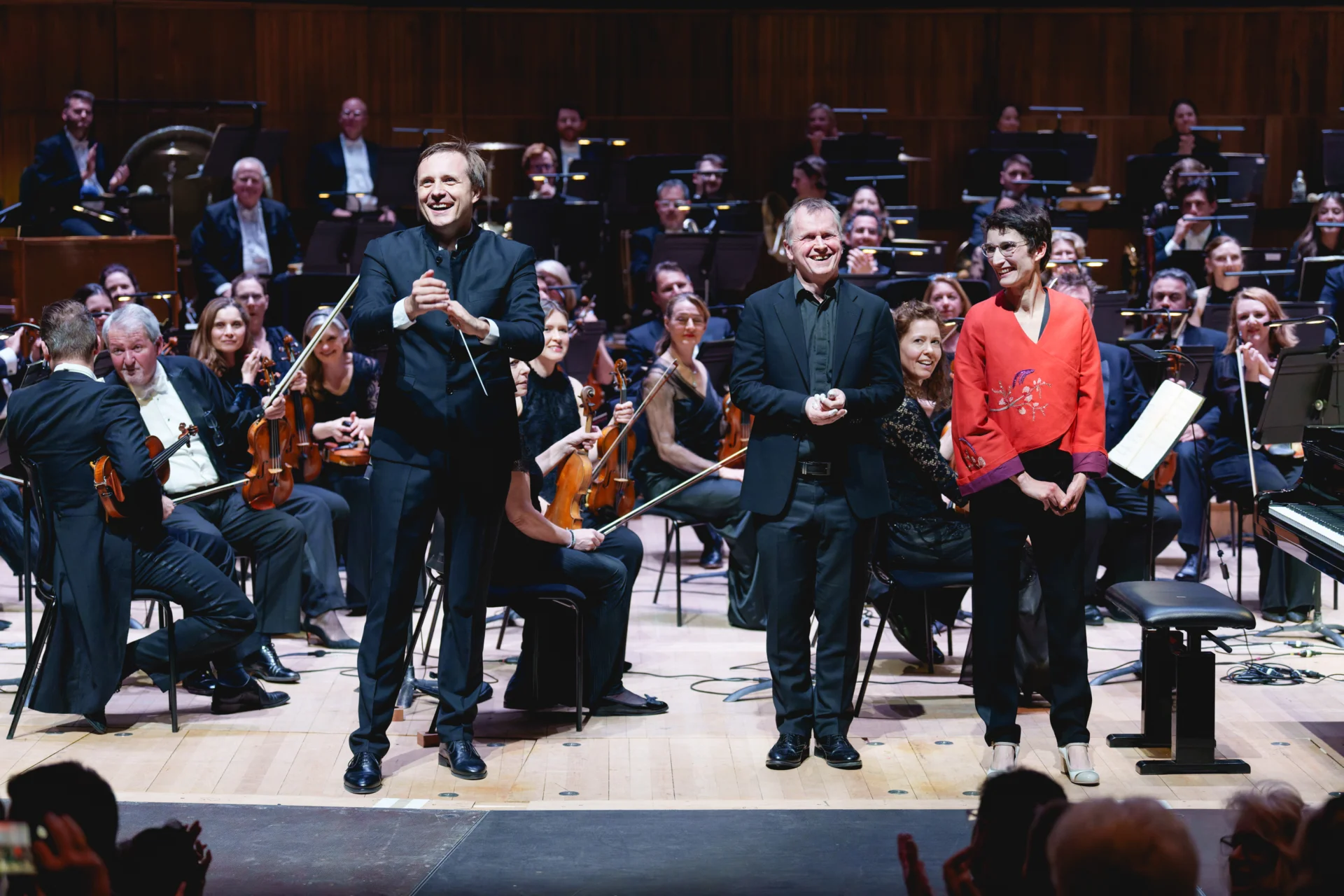 Vasily Petrenko, Steven Osborne and Cecile Lartigau standing and smiling at the front of the stage as they receive applause