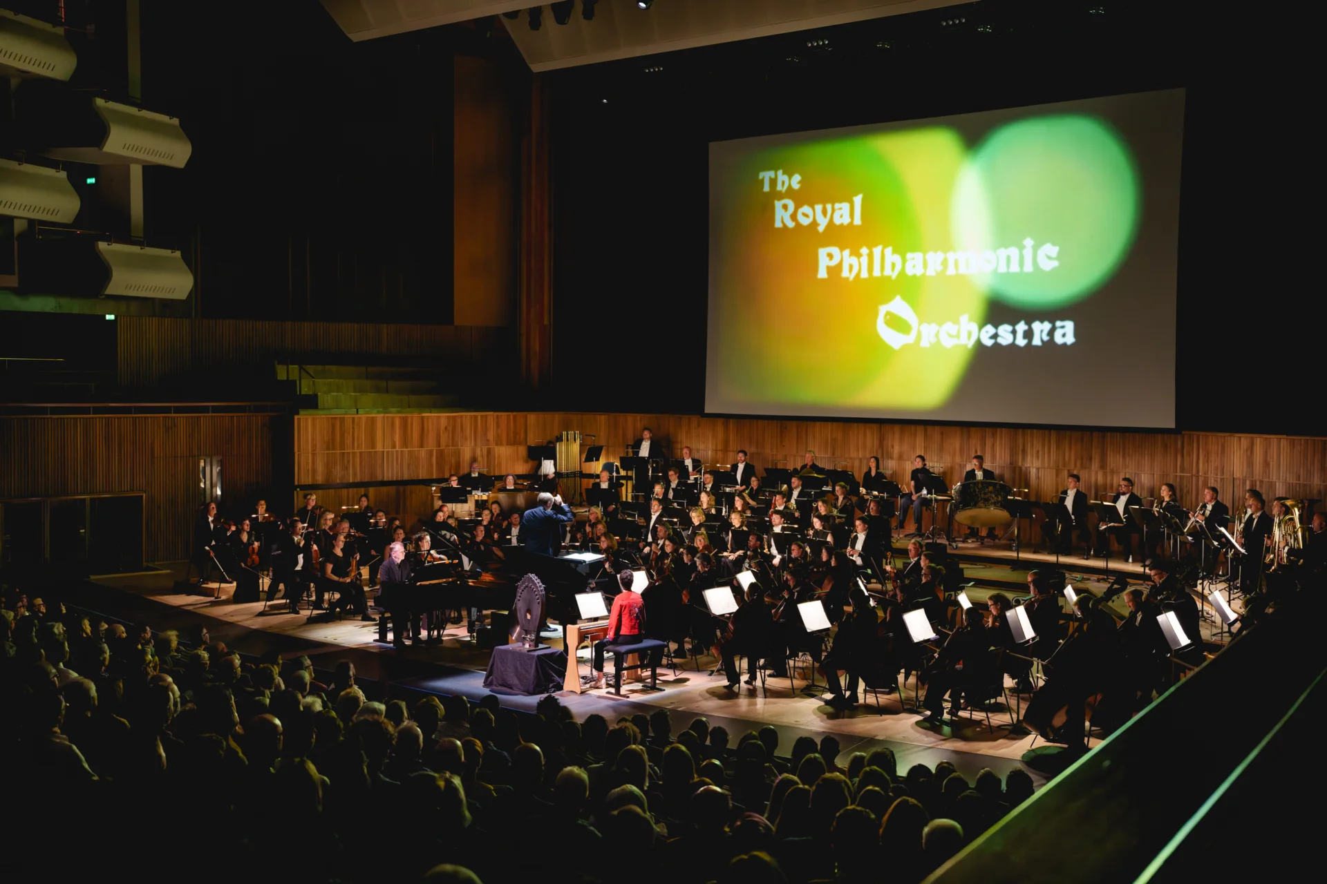 The RPO performing on stage at the Royal Festival Hall. The screen behind the Orchestra has colourful circles with the Orchestra's name