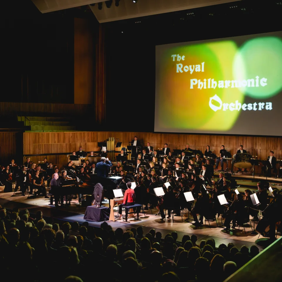 The RPO performing on stage at the Royal Festival Hall. The screen behind the Orchestra has colourful circles with the Orchestra's name