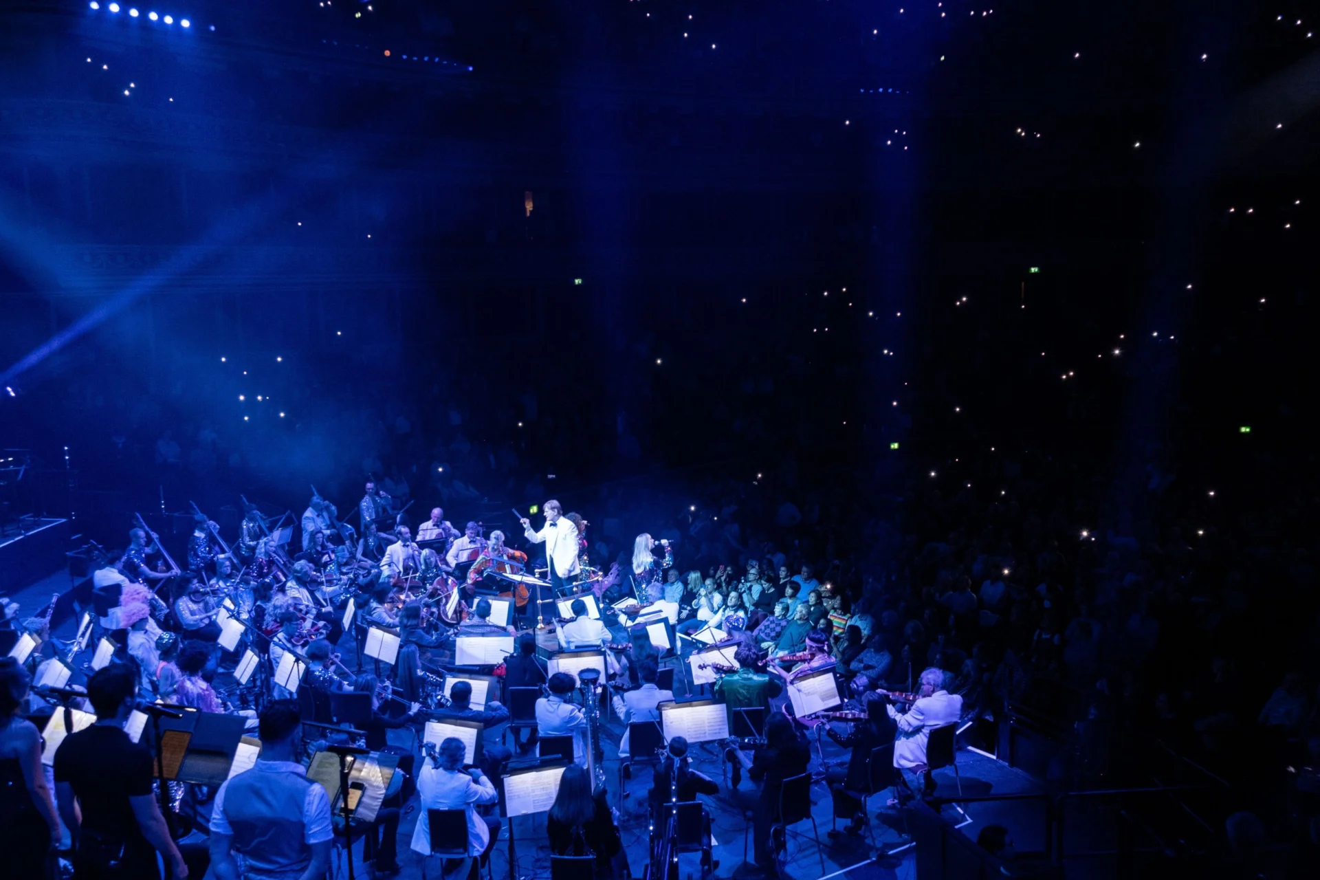 Matthew Freeman perform an ABBAphonic concert at the Royal Albert Hall, basked in blue light with a shimmering audience behind them