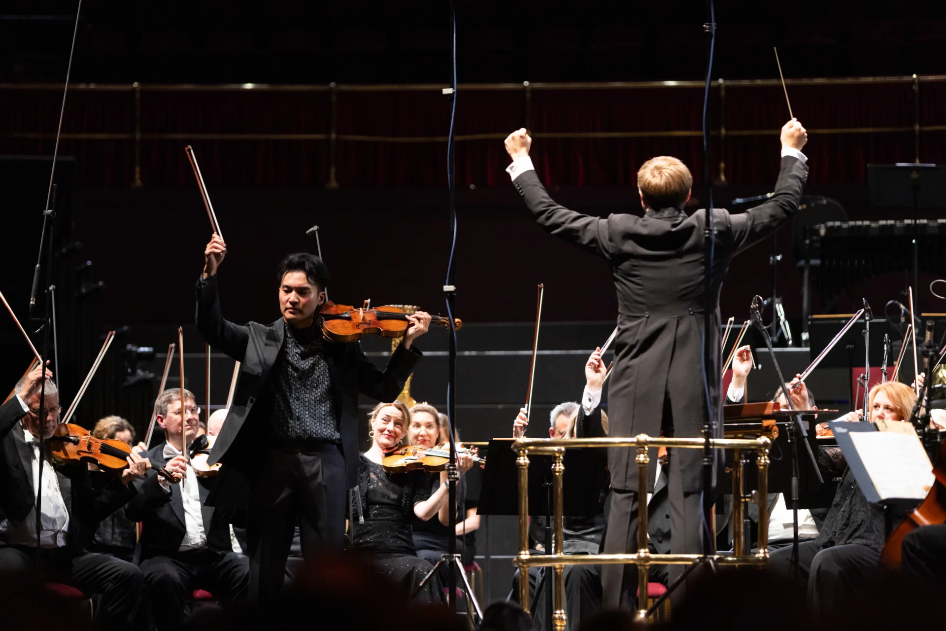 Ray Chen and the Orchestra string players raising their bows as Vasily raises his hands for a final note