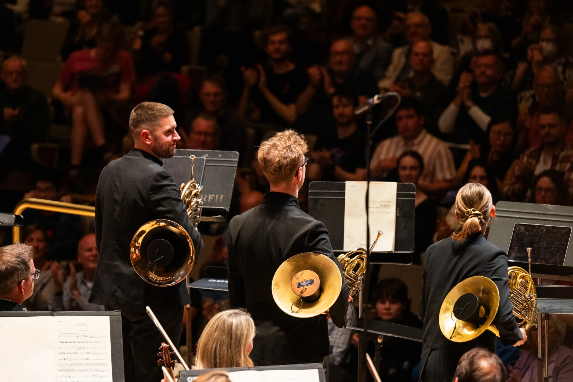 The three horn players receiving applause taken from behind them, with Ben Hulme smiling and looking at the others