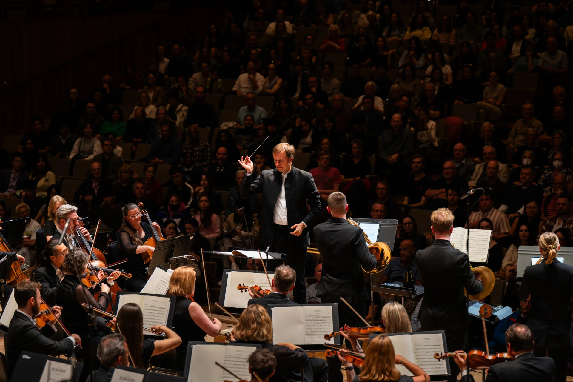 Vasily Petrenko conducting the Royal Philharmonic Orchestra on stage at the Royal Festival Hall, with three horn player soloists at the front of the stage