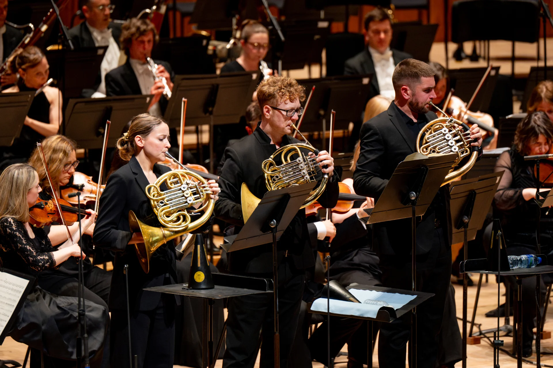 The three horn soloists playing on stage