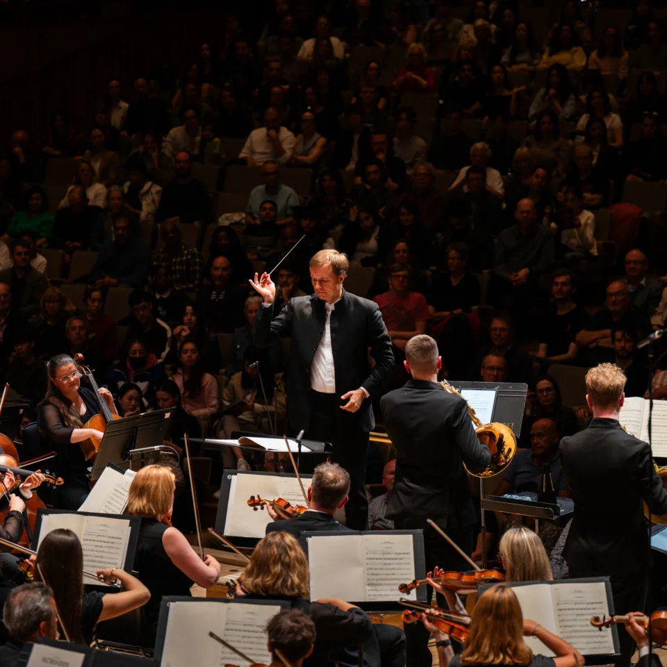 Vasily Petrenko conducting the Royal Philharmonic Orchestra on stage at the Royal Festival Hall, with three horn player soloists at the front of the stage