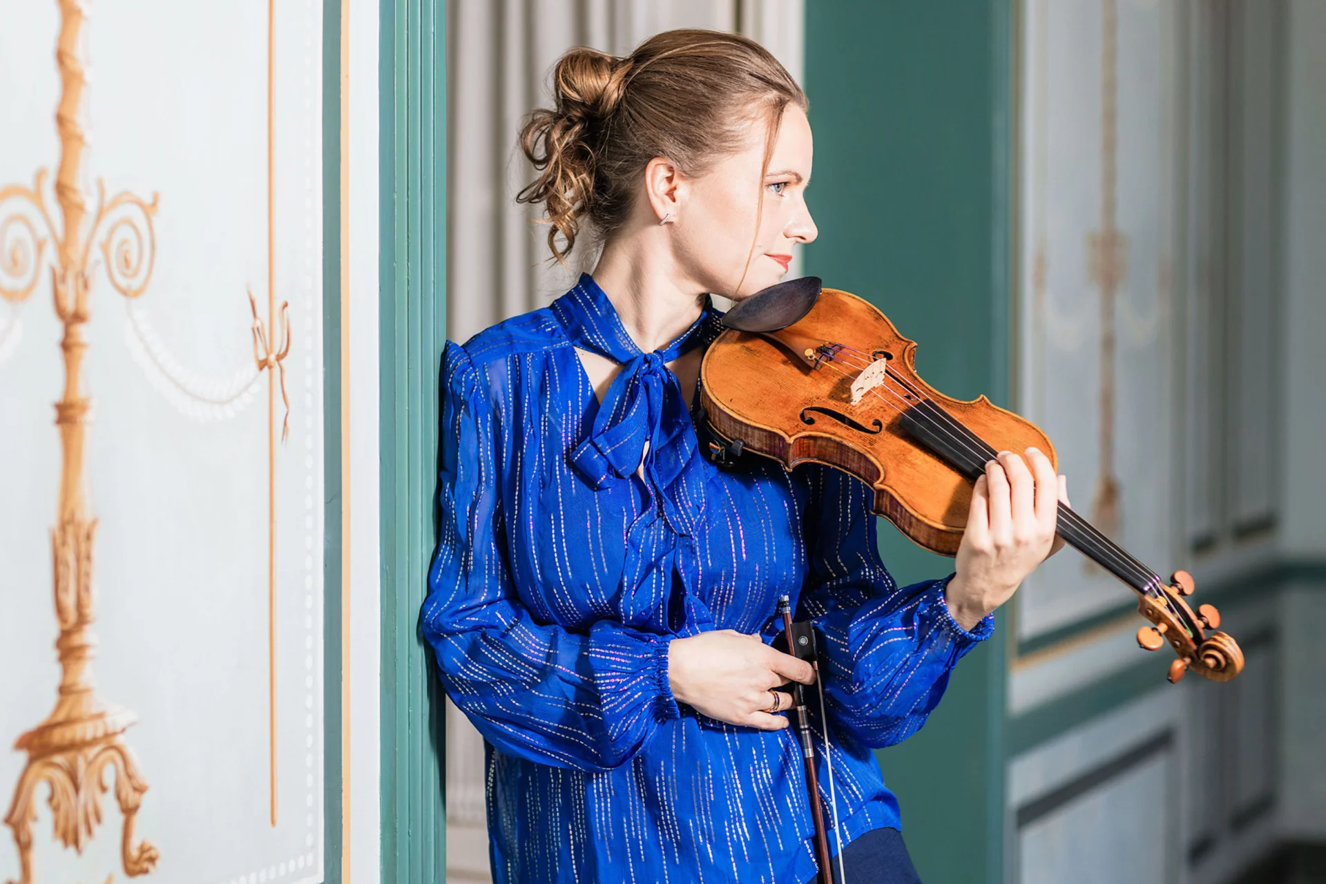Julia Fischer in a blue top and holding her violin looking away from the camera