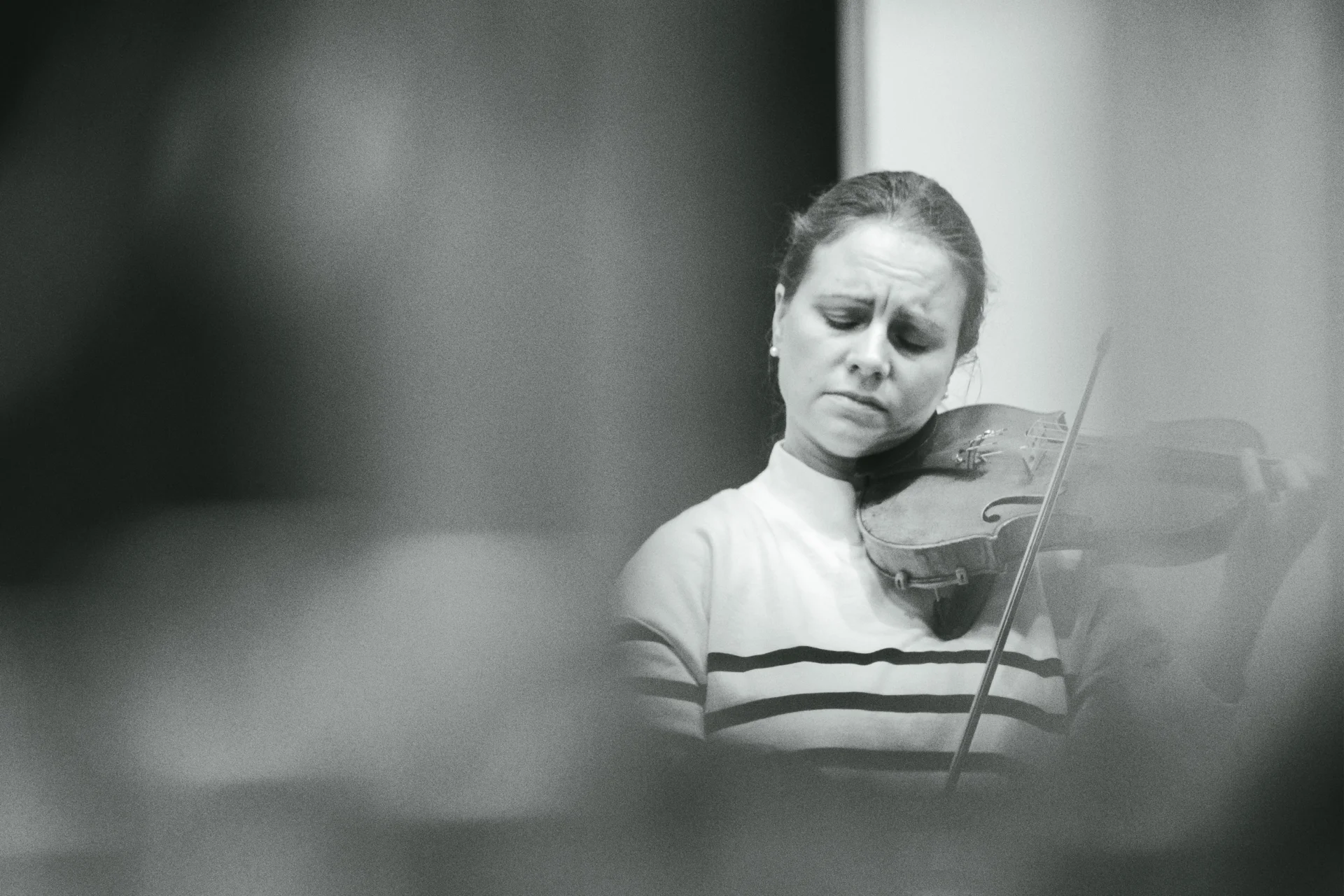 A black and white photo Julia Fischer playing her violin in rehearsal seen through a harp