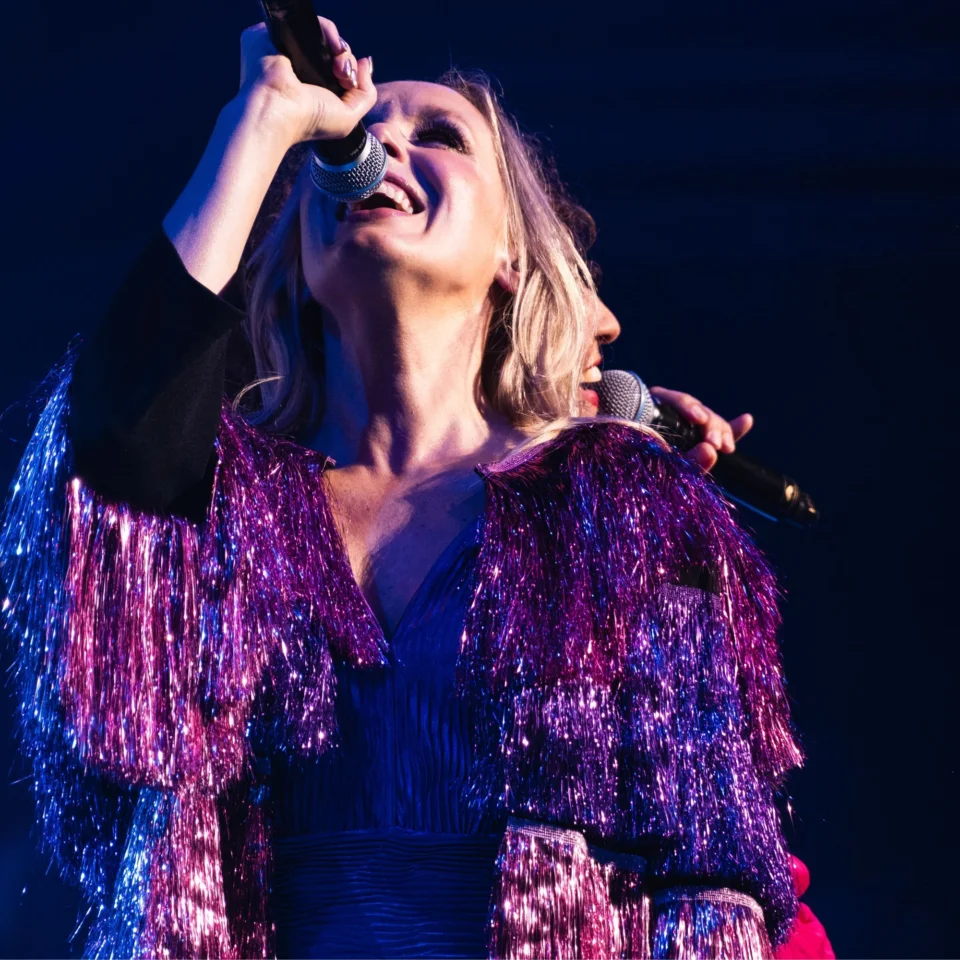 ABBAphonic vocalist sings into microphone wearing glittery purple flaires