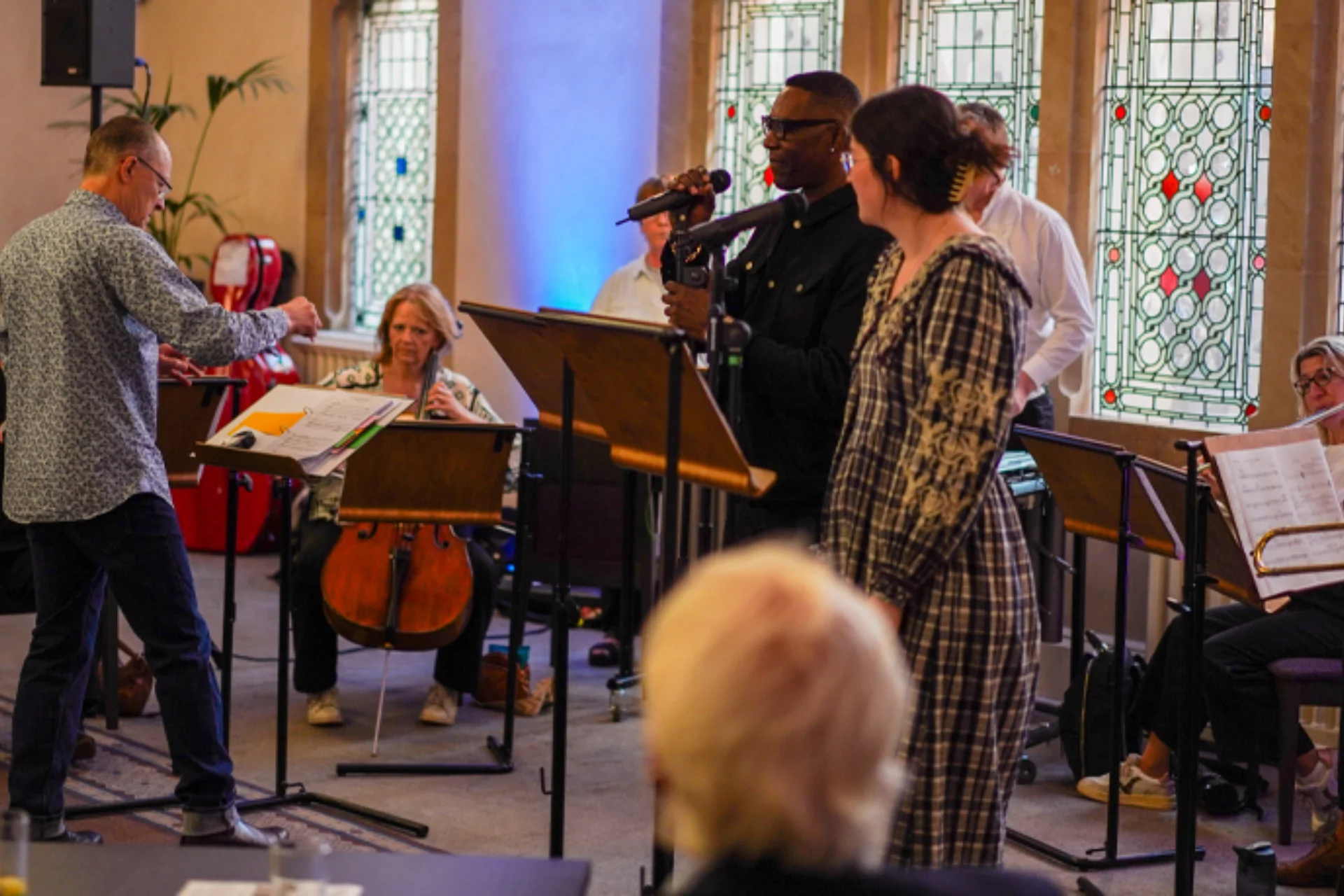 A man and a woman performing in front of a small group of RPO musicians in the foyer of Cadogan Hall
