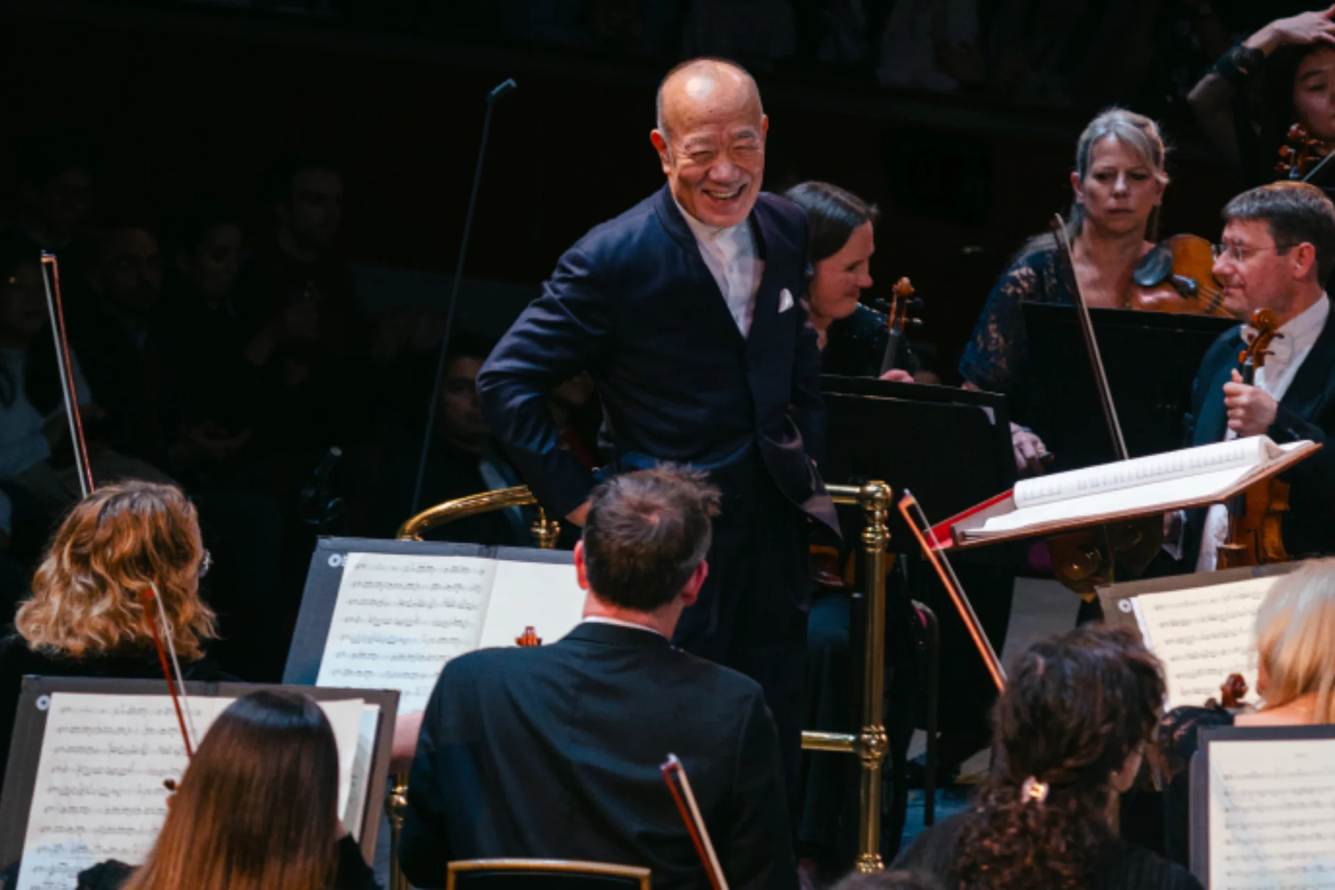 Joe Hisaishi smiling widely on the podium of the Royal Albert Hall as he looks at the second violins