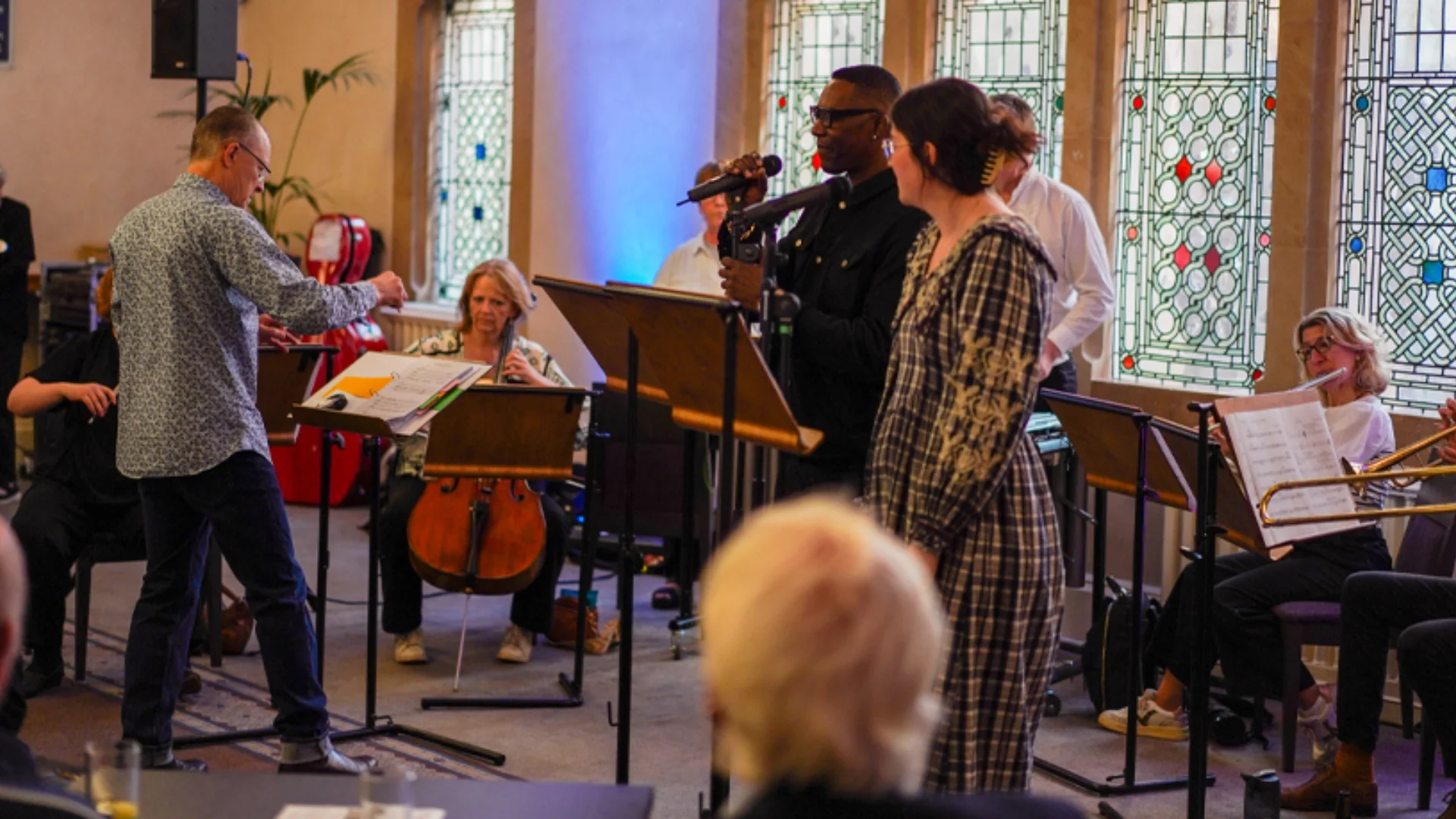 A man and a woman performing in front of a small group of RPO musicians in the foyer of Cadogan Hall