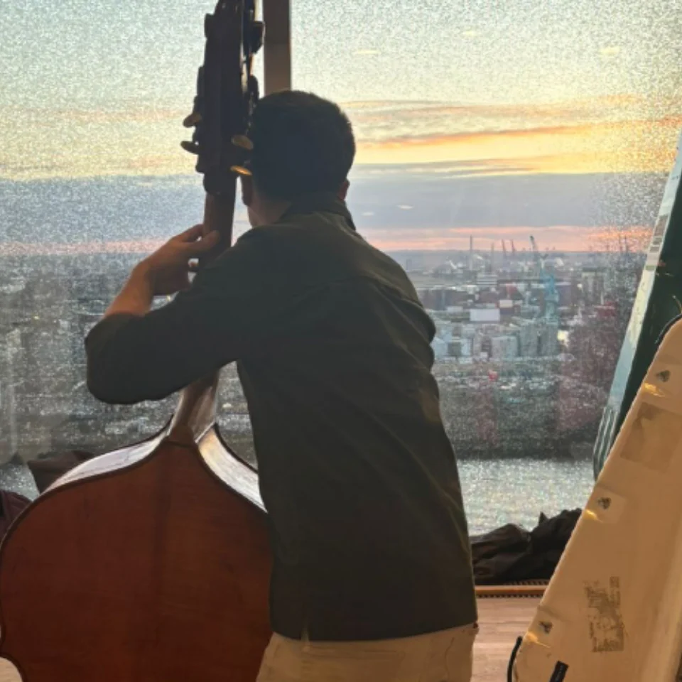 A double bass player practicing while looking out over a sunset in Hamburg
