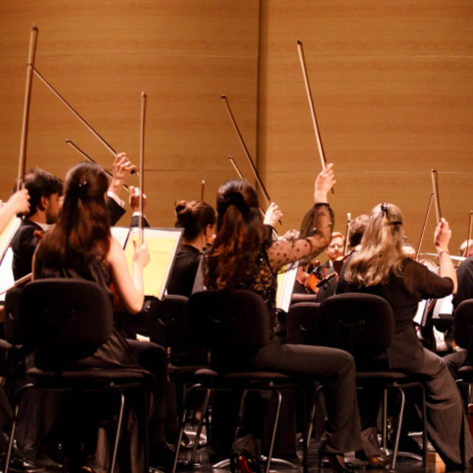 The first violins raising their bows in the air after playing a final note, and conductor Vasily Petrenko standing on the podium and smiling