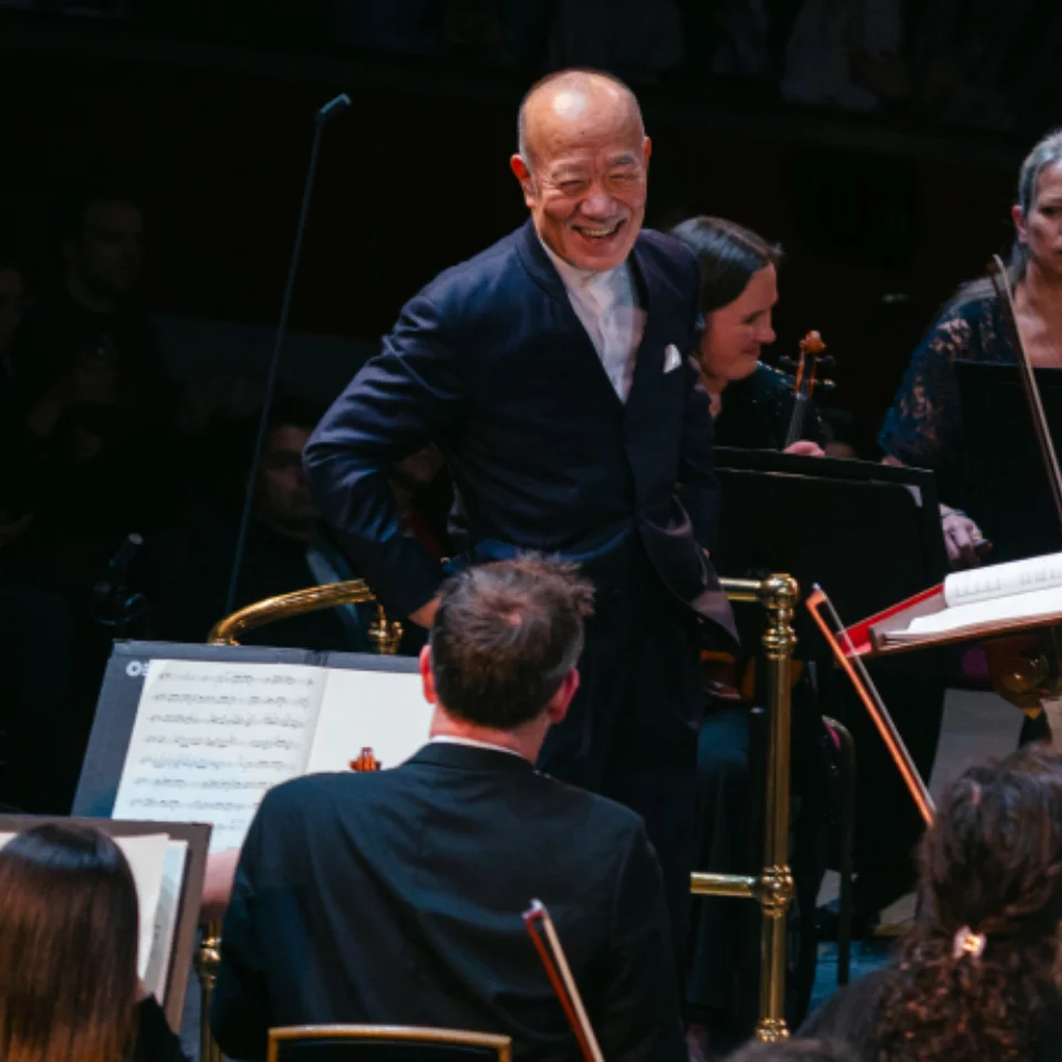 Joe Hisaishi smiling widely on the podium of the Royal Albert Hall as he looks at the second violins