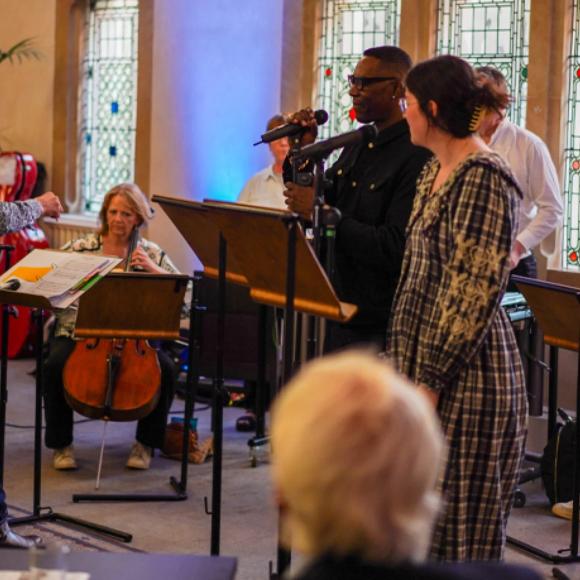 A man and a woman performing in front of a small group of RPO musicians in the foyer of Cadogan Hall