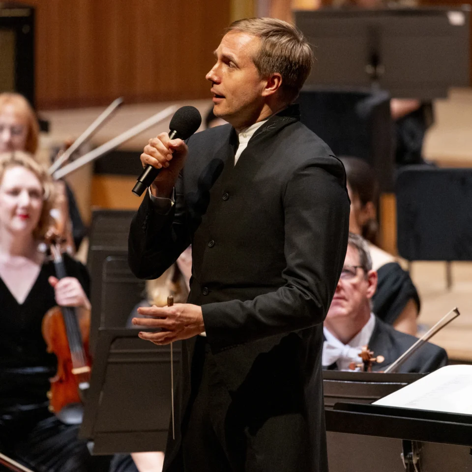 Vasily Petrenko stands ion stage in front of the Orchestra, speaking about the repertoire to the audience