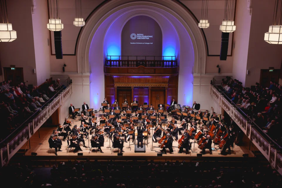 The Royal Philharmonic Orchestra performs onstage at Cadogan Hall. The Hall has tall ceilings and rounded archways.