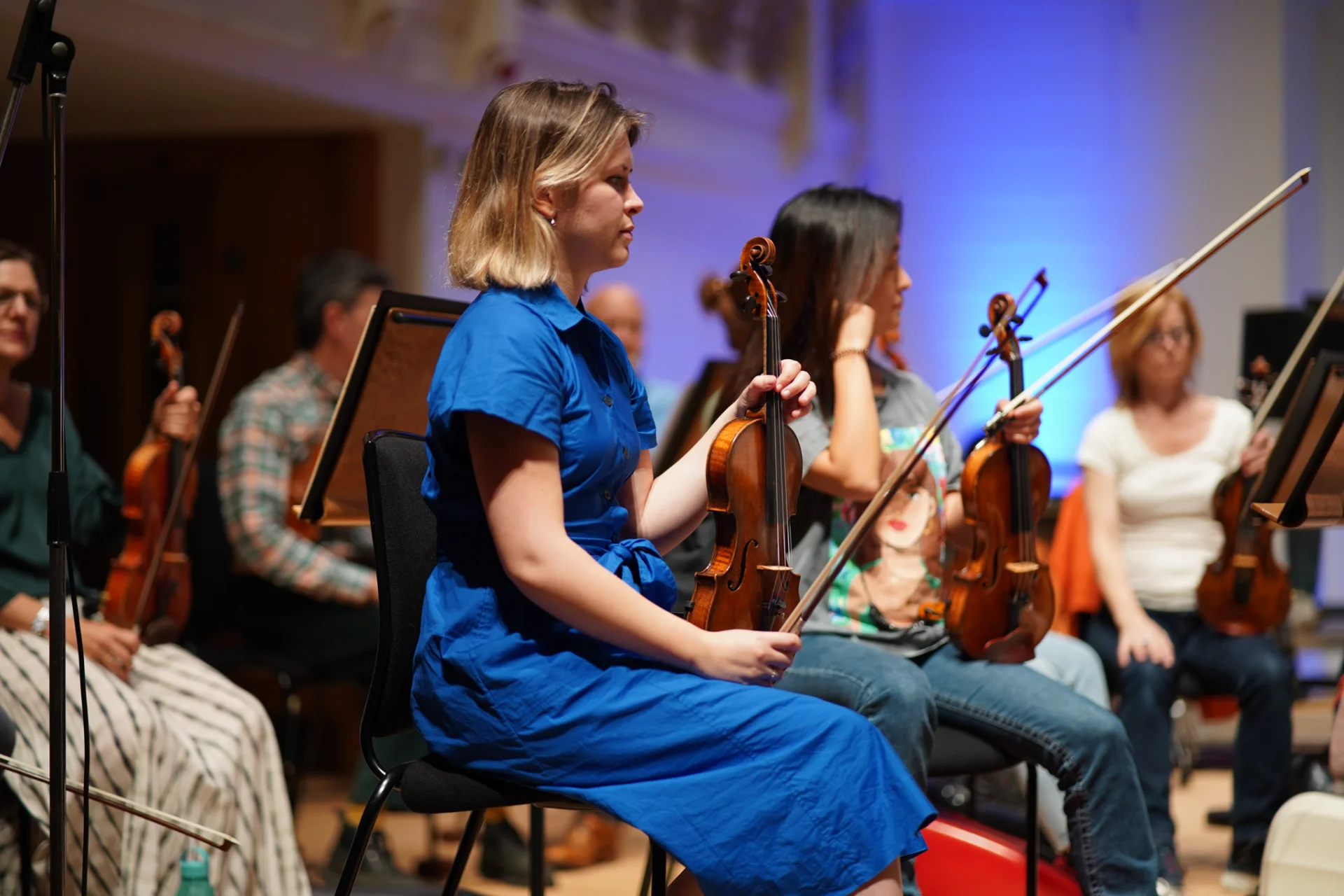 A viola player in a blue dress sits in rehearsal at Cadogan Hall