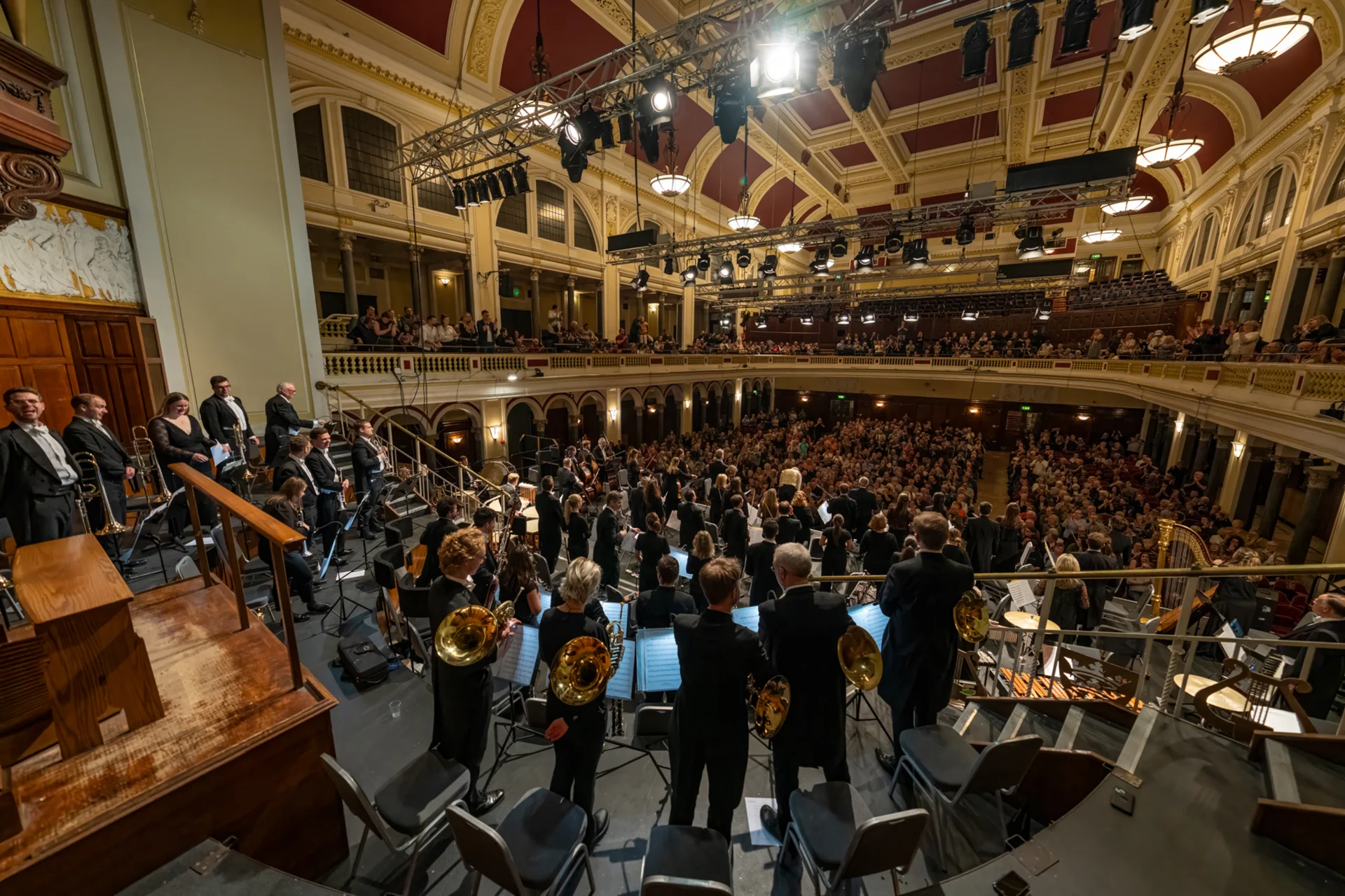 A wide fisheye lens shot from behind the Orchestra as they stand on stage in Hull City Hall for applause