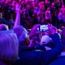 An audience on their feet at a pop show at the Royal Albert Hall. Someone is videoing it on their phone.