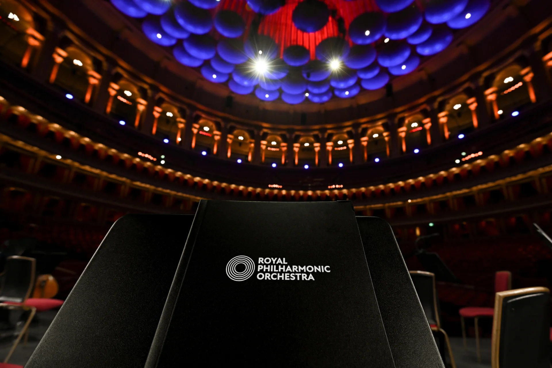 Close up shot of a Royal Philharmonic Orchestra score book on a music stand, with the Royal Albert Hall in the background
