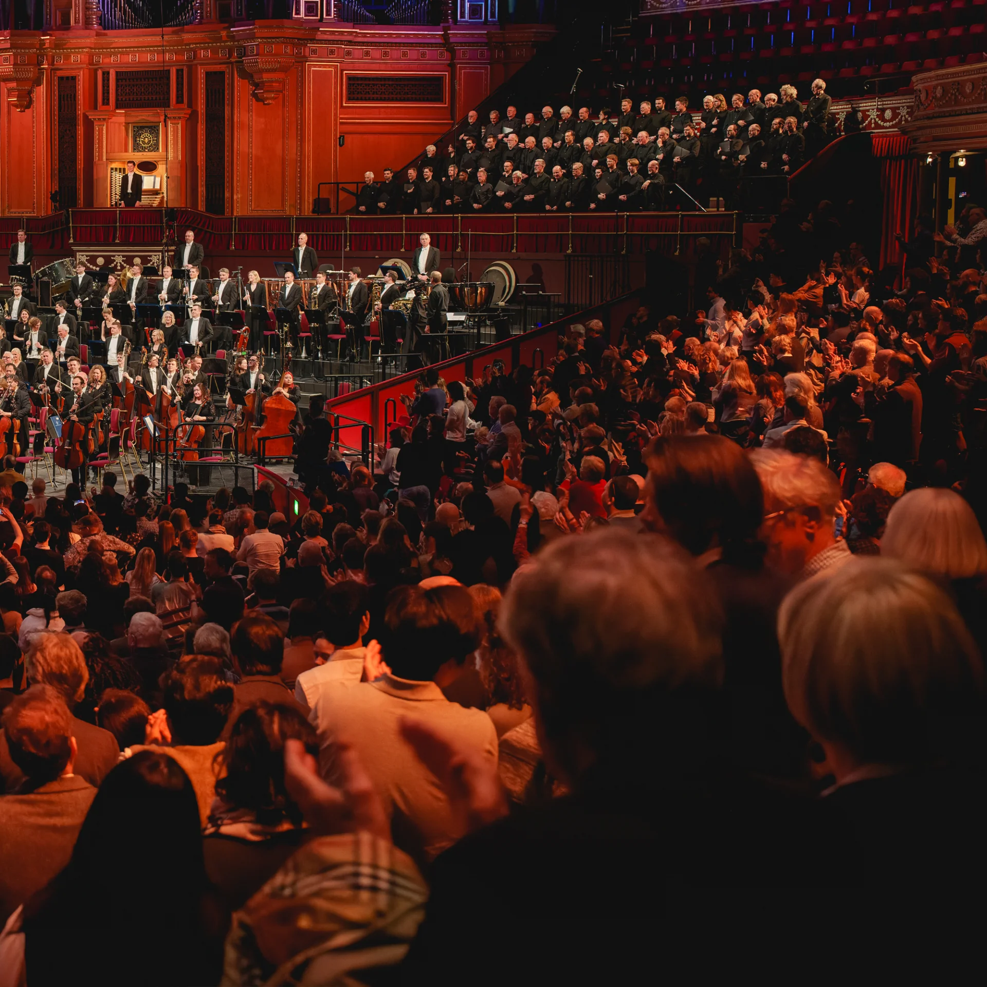 Audience members standing to applause as the Orchestra and a choir stands on stage and in the choir stalls at the Royal Albert Hall