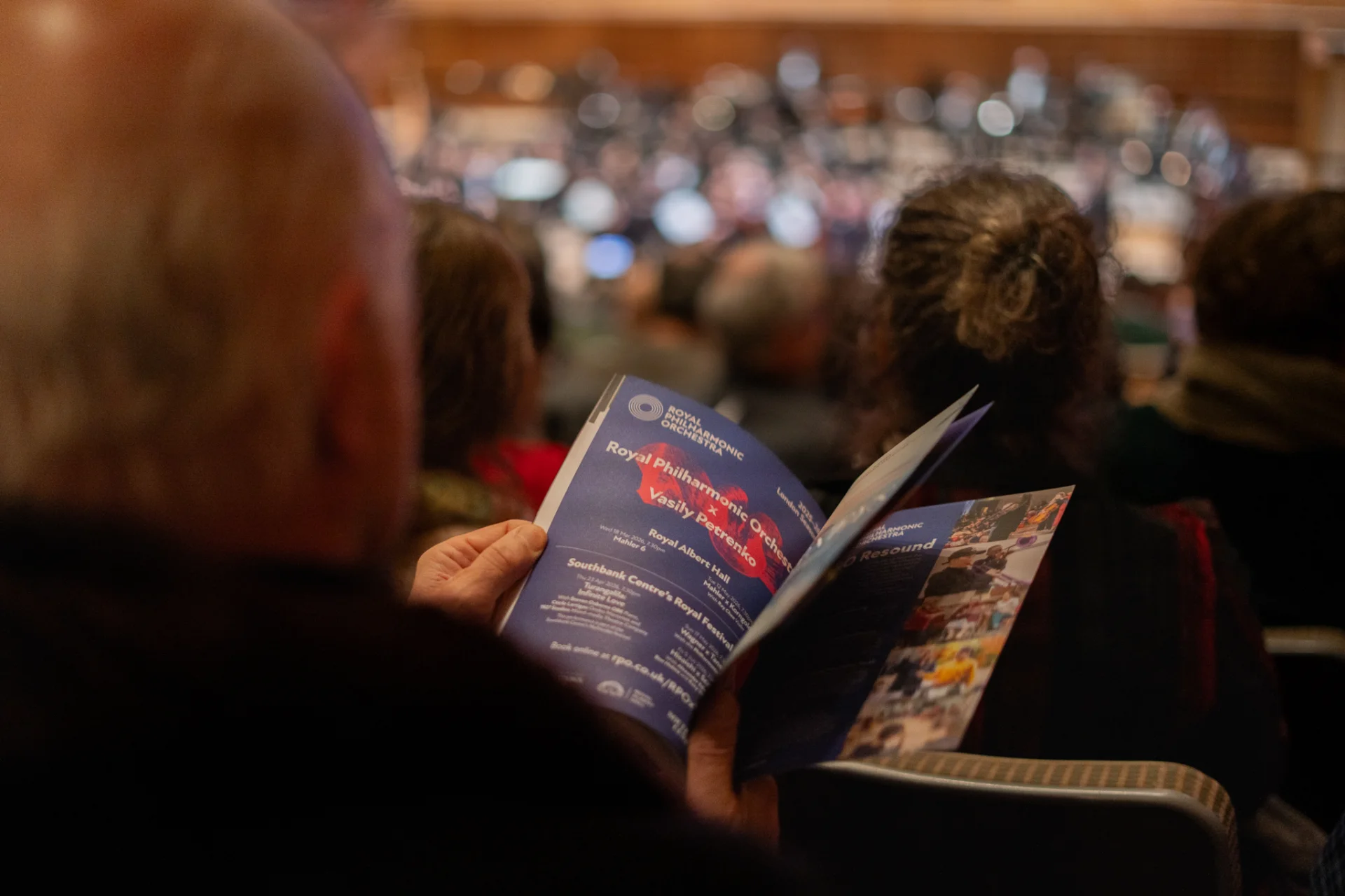 Close up of an audience member at the Royal Festival Hall, looking through the programme of a Royal Philharmonic Orchestra performance