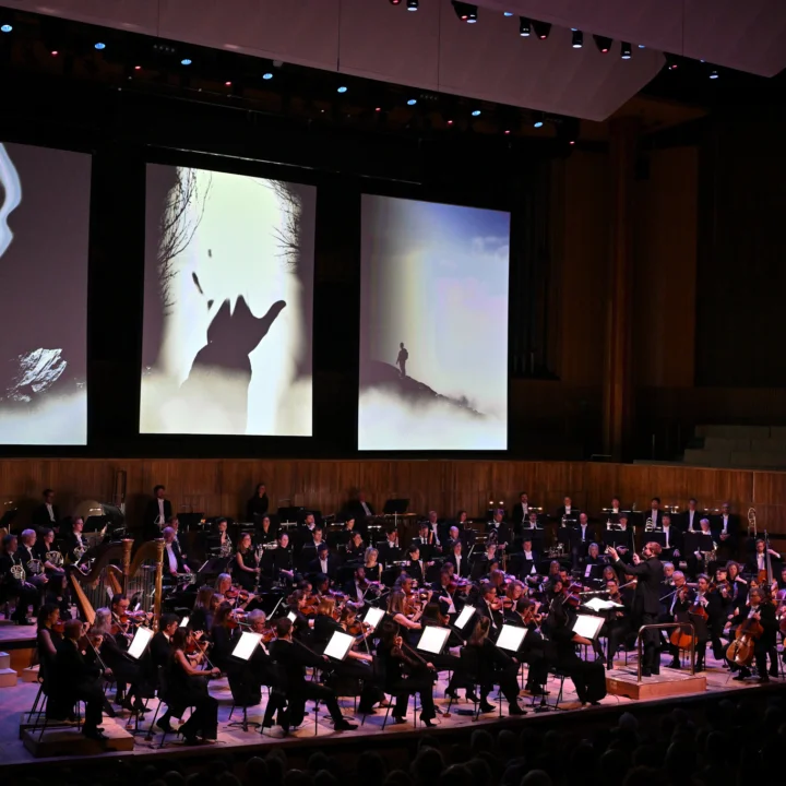 The Royal Philharmonic Orchestra performing onstage at the Royal Festival Hall. Behind them are projections of a colourful graphic film.