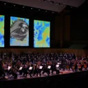 The RPO conducted by Vasily Petrenko on stage at the Royal Festival Hall, with three screens behind the stage showing a blue and yellow cloudy artwork with a huge silver eye in the centre