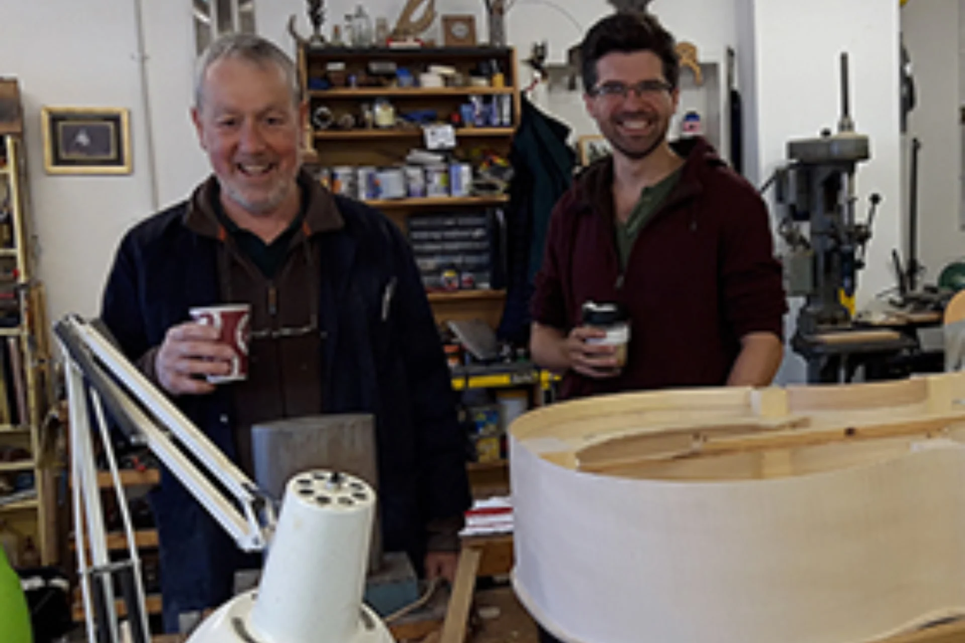 2 men holding coffee in front of a Double Bass that is being built